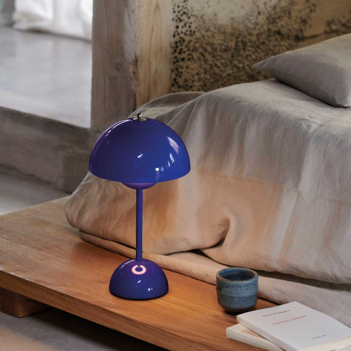 Blue lamp on a wooden nightstand next to a bed with pillows and a book.