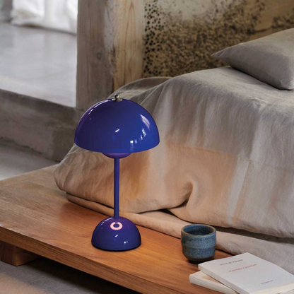 Blue lamp on a wooden nightstand next to a bed with pillows and a book.