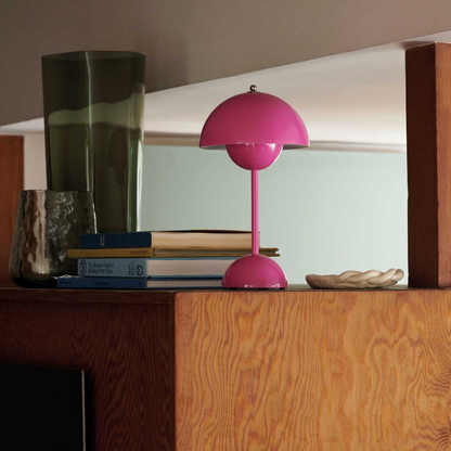 Pink table lamp on a wooden surface with books and a green vase in the background
