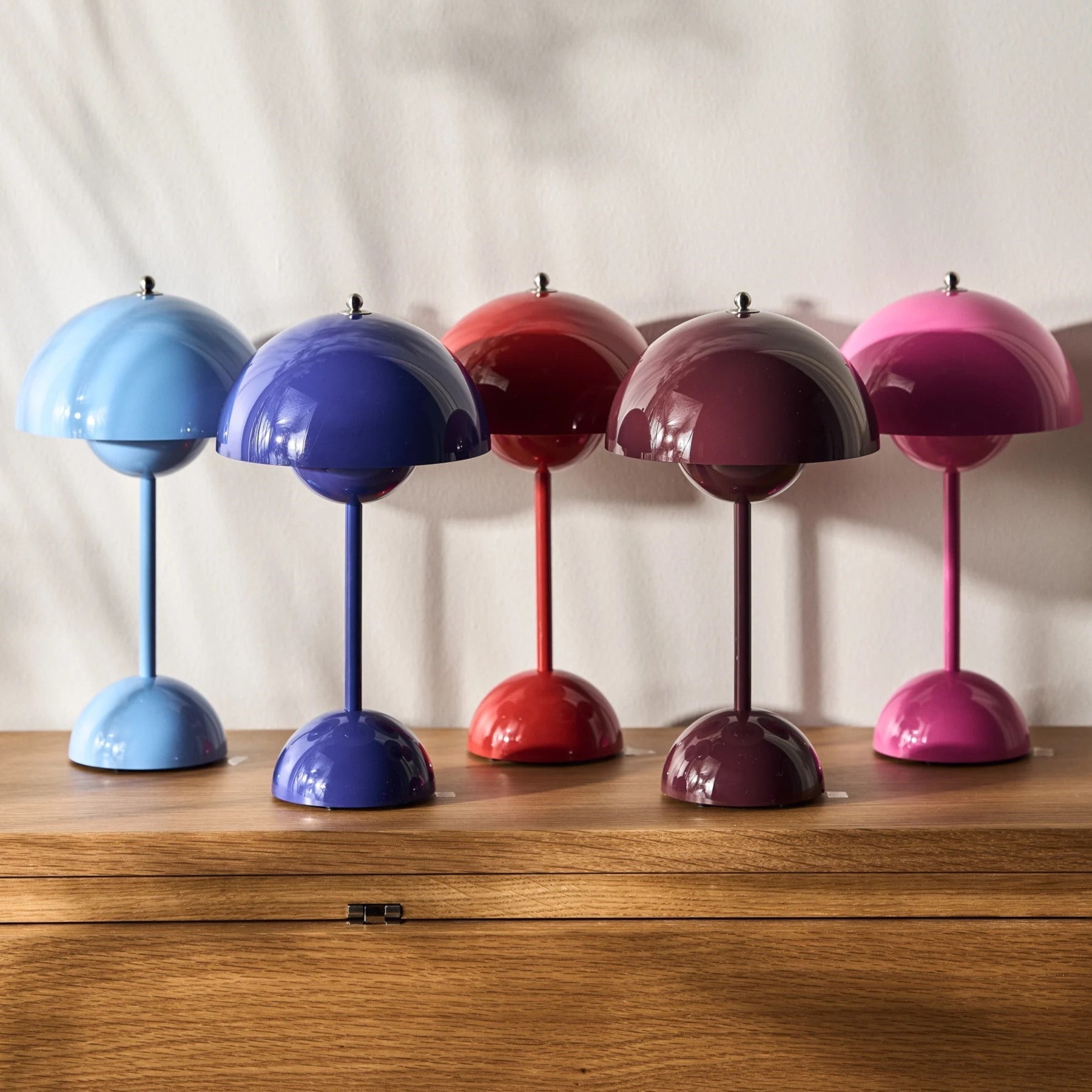 Five colorful table lamps on a wooden surface with a neutral background