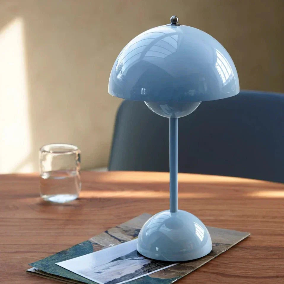 Blue table lamp on a wooden surface with a glass of water and a magazine in the background.