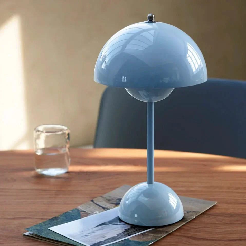 Blue table lamp on a wooden surface with a glass of water and a magazine in the background.