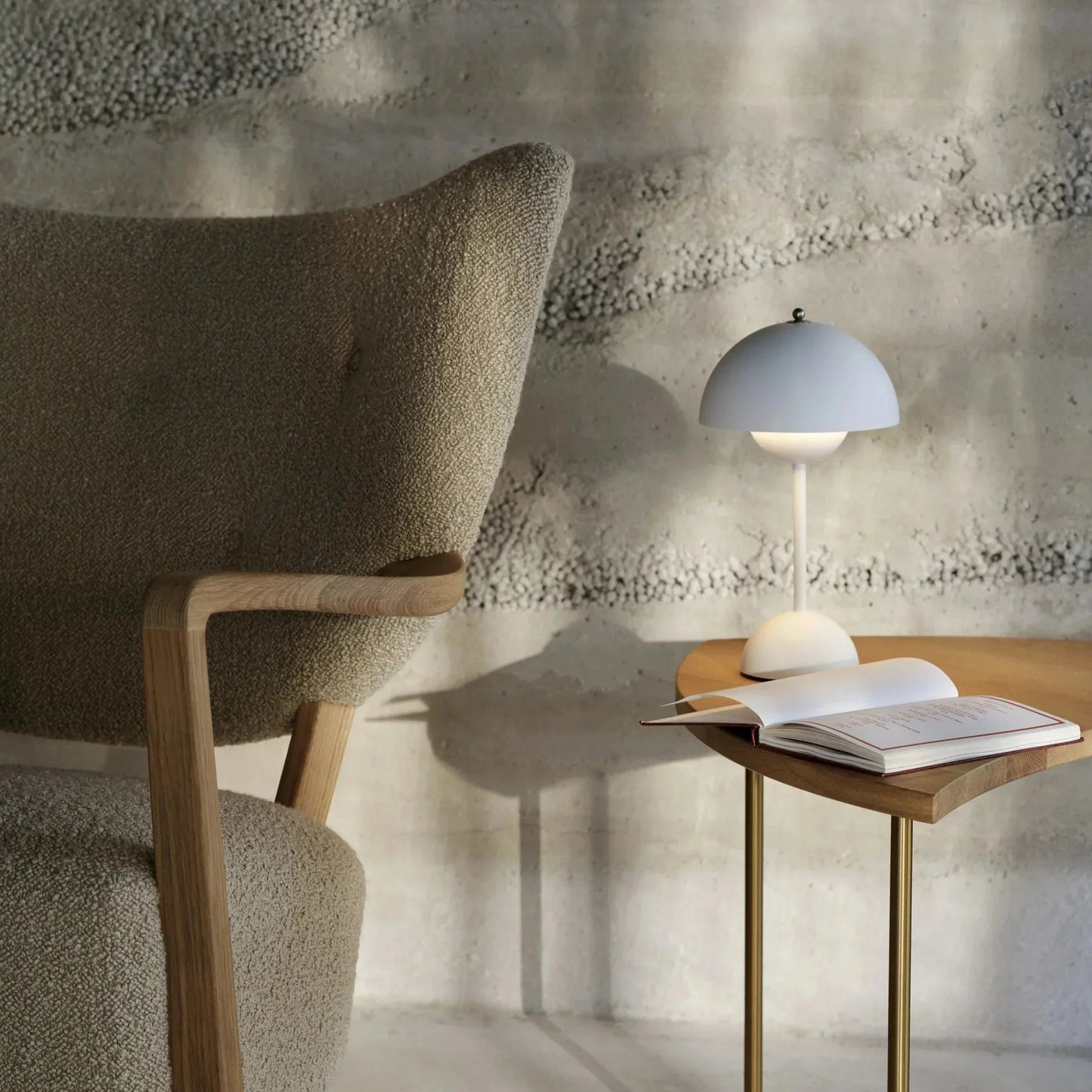 Modern chair next to a side table with a lamp and open book against a textured wall.