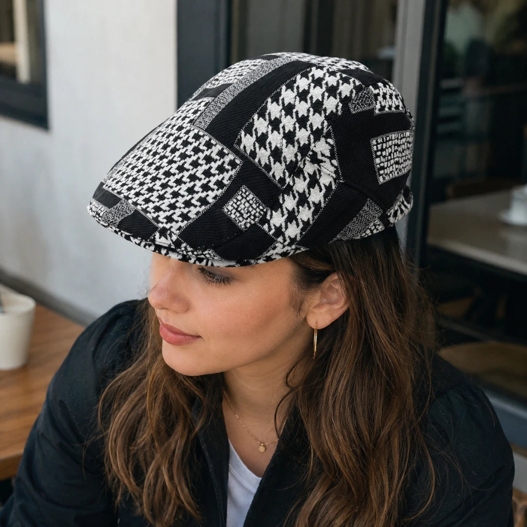 Josh & Tate - MosaicBrim™ Patchwork Flat Cap - A woman wearing a black and white patterned flat cap with houndstooth, patchwork, and textured block designs, photographed in a cafe setting.
