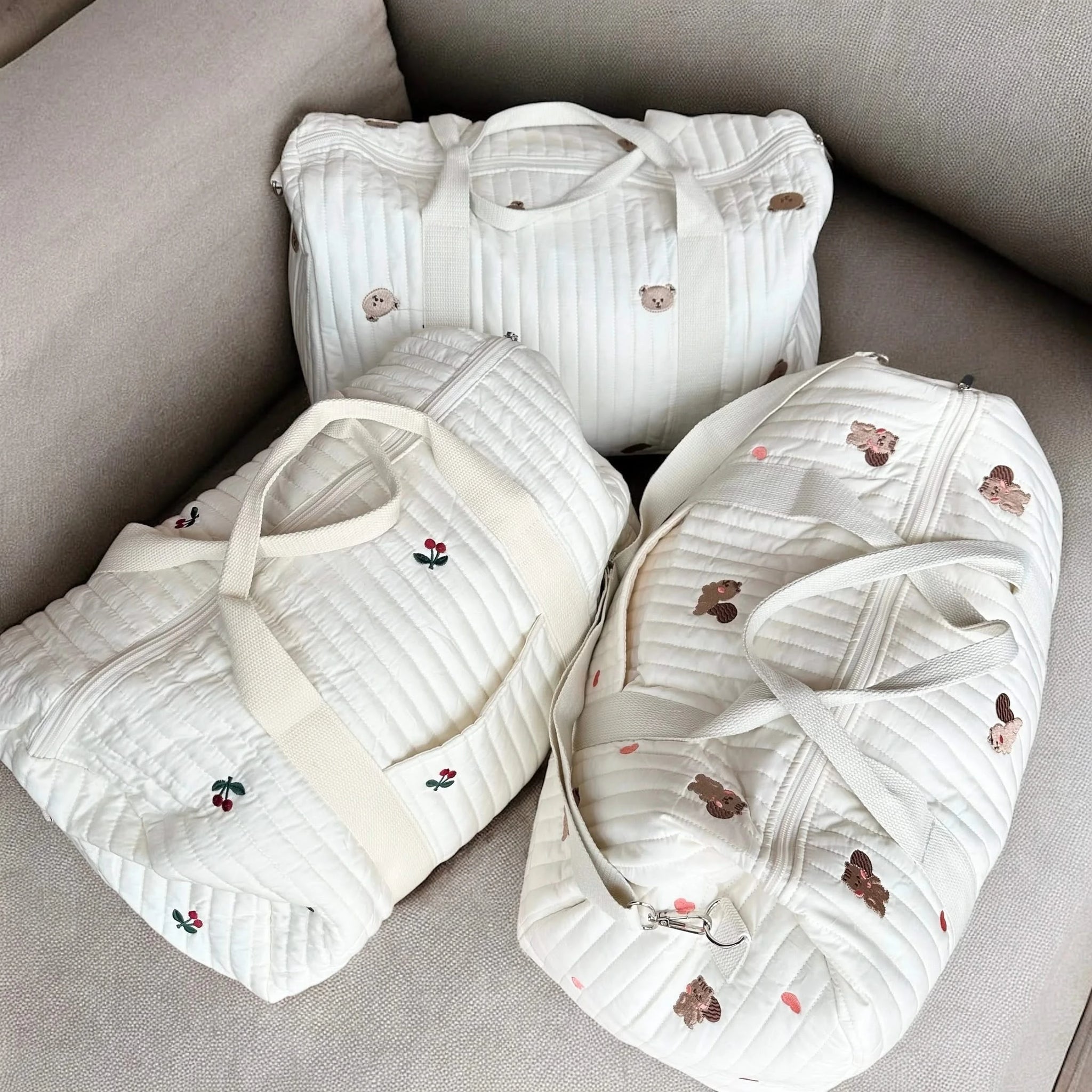 Josh & Tate - Mum On The Go Duffle Bag - Three white baby bibs with embroidery on a gray surface