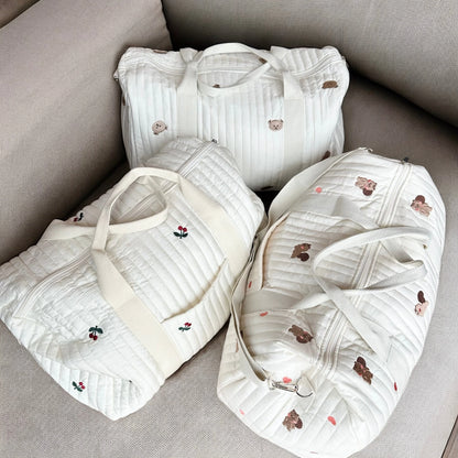 Josh & Tate - Mum On The Go Duffle Bag - Three white baby bibs with embroidery on a gray surface
