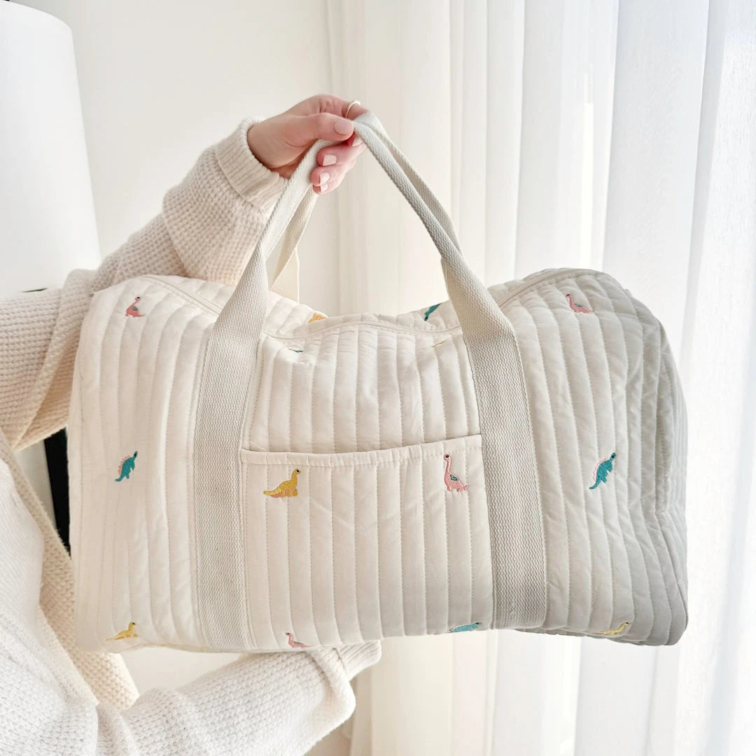 Josh & Tate - Mum On The Go Duffle Bag - Person holding a quilted bag with small embroidered designs against a white curtain background