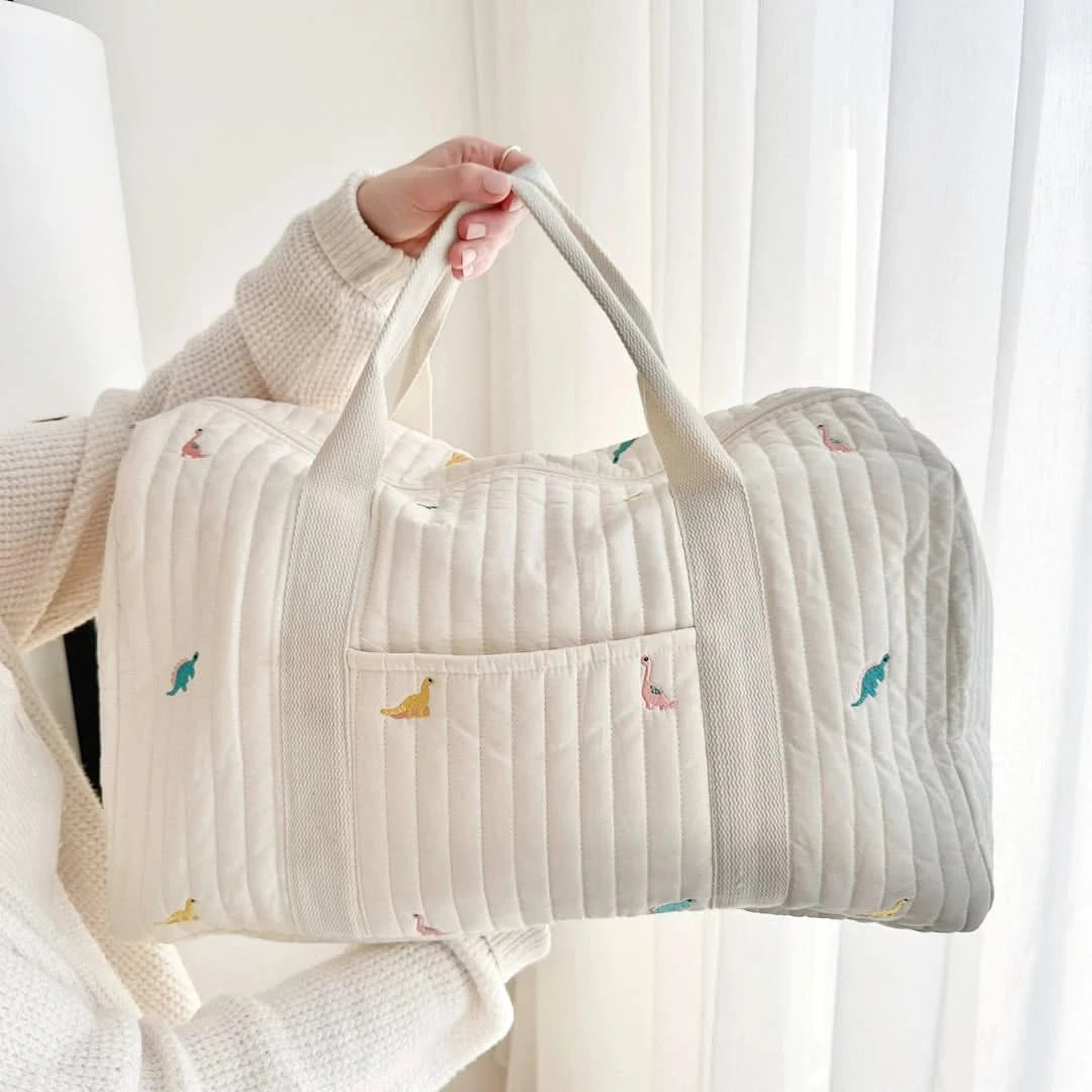 Josh & Tate - Mum On The Go Duffle Bag - Person holding a quilted bag with small embroidered designs against a white curtain background