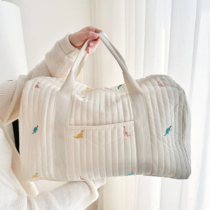 Josh & Tate - Mum On The Go Duffle Bag - Person holding a quilted bag with small embroidered designs against a white curtain background