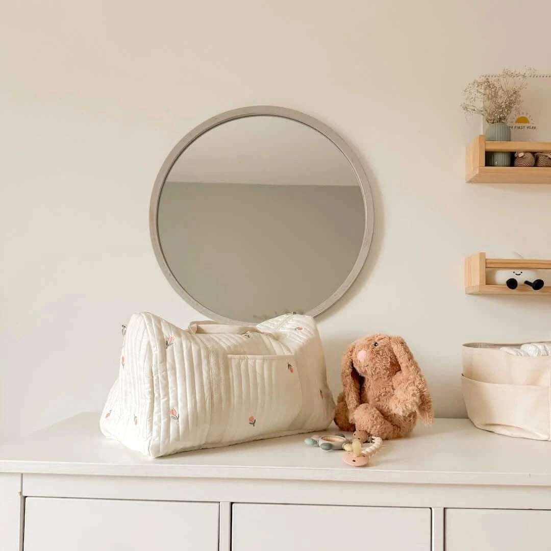 Josh & Tate - Mum On The Go Duffle Bag - White quilted bag on a dresser with a round mirror and toys in a nursery setting.