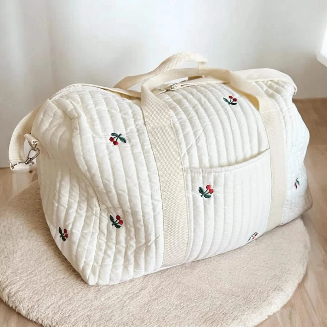 Josh & Tate - Mum On The Go Duffle Bag - White quilted duffel bag with embroidered designs on a wooden surface