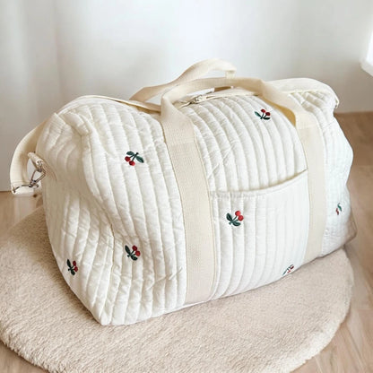 Josh & Tate - Mum On The Go Duffle Bag - White quilted duffel bag with embroidered designs on a wooden surface