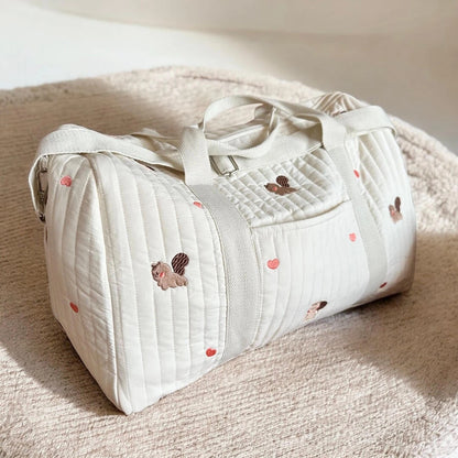 Josh & Tate - Mum On The Go Duffle Bag - White quilted duffel bag with embroidered designs on a beige surface