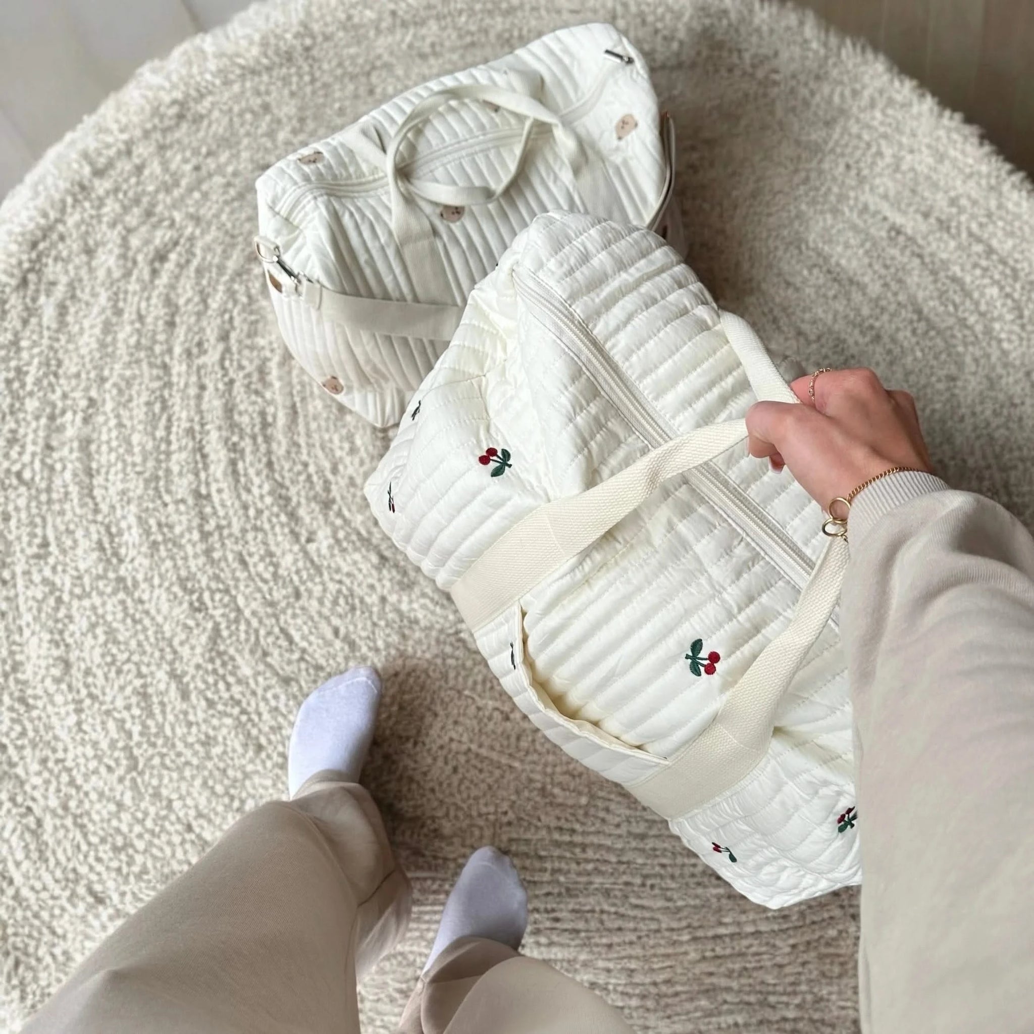 Josh & Tate - Mum On The Go Duffle Bag - Person holding a white quilted bag with floral embroidery on a textured surface