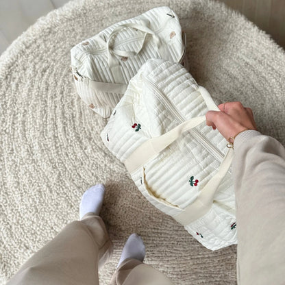 Josh & Tate - Mum On The Go Duffle Bag - Person holding a white quilted bag with floral embroidery on a textured surface