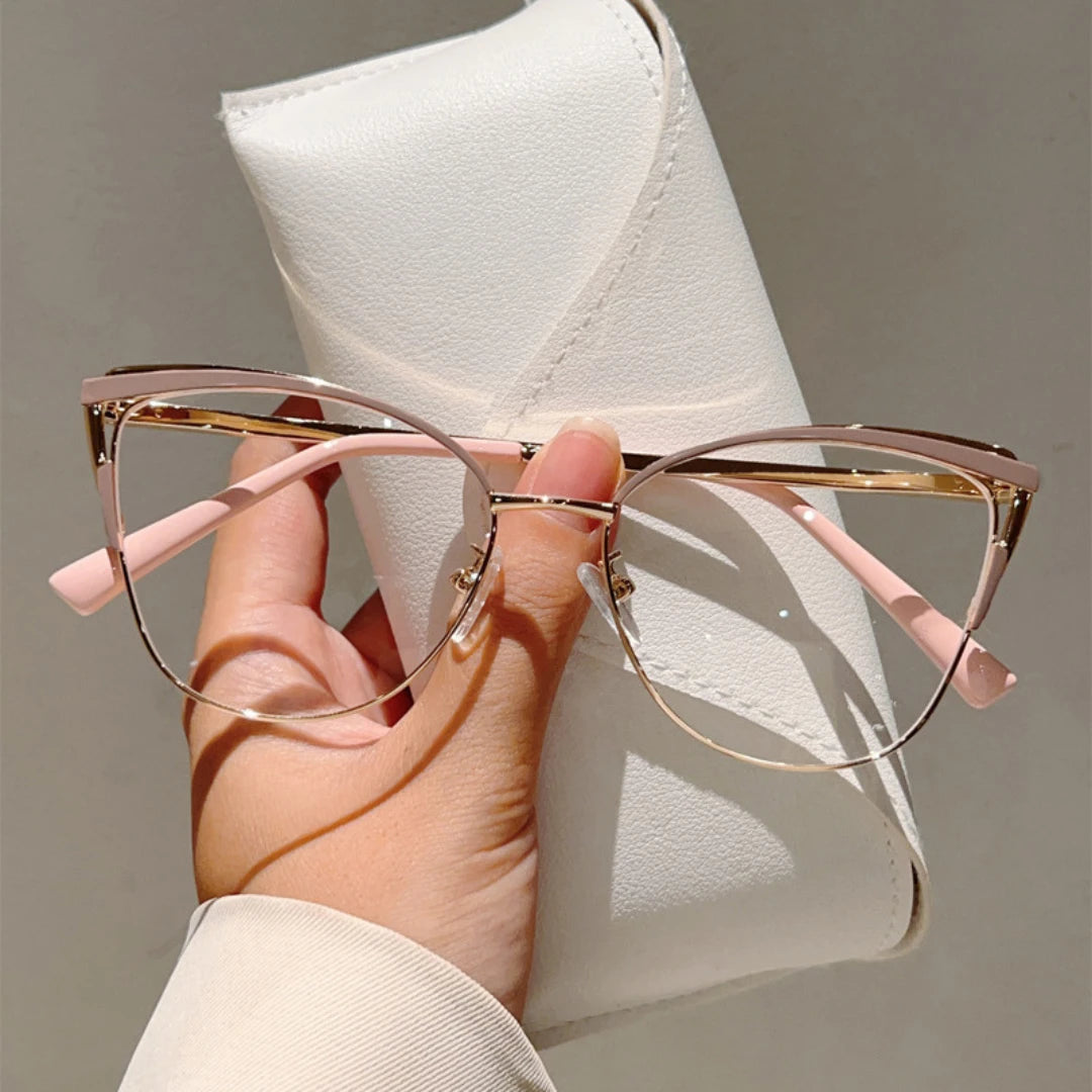 Hand holding a pair of cat-eye glasses with gold frames against a white case.