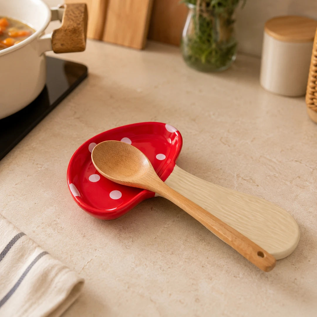 Josh & Tate - MushPerch™ Kitchen Spoon Holder - A red ceramic spoon rest with white polka dots and a natural wood spoon resting on top, set on a beige kitchen countertop.