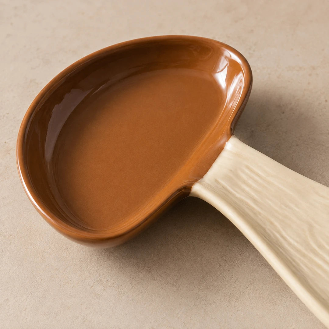 Josh & Tate - MushPerch™ Kitchen Spoon Holder - A ceramic serving spoon with a glossy brown bowl and a textured off-white handle, shown on a neutral beige background.