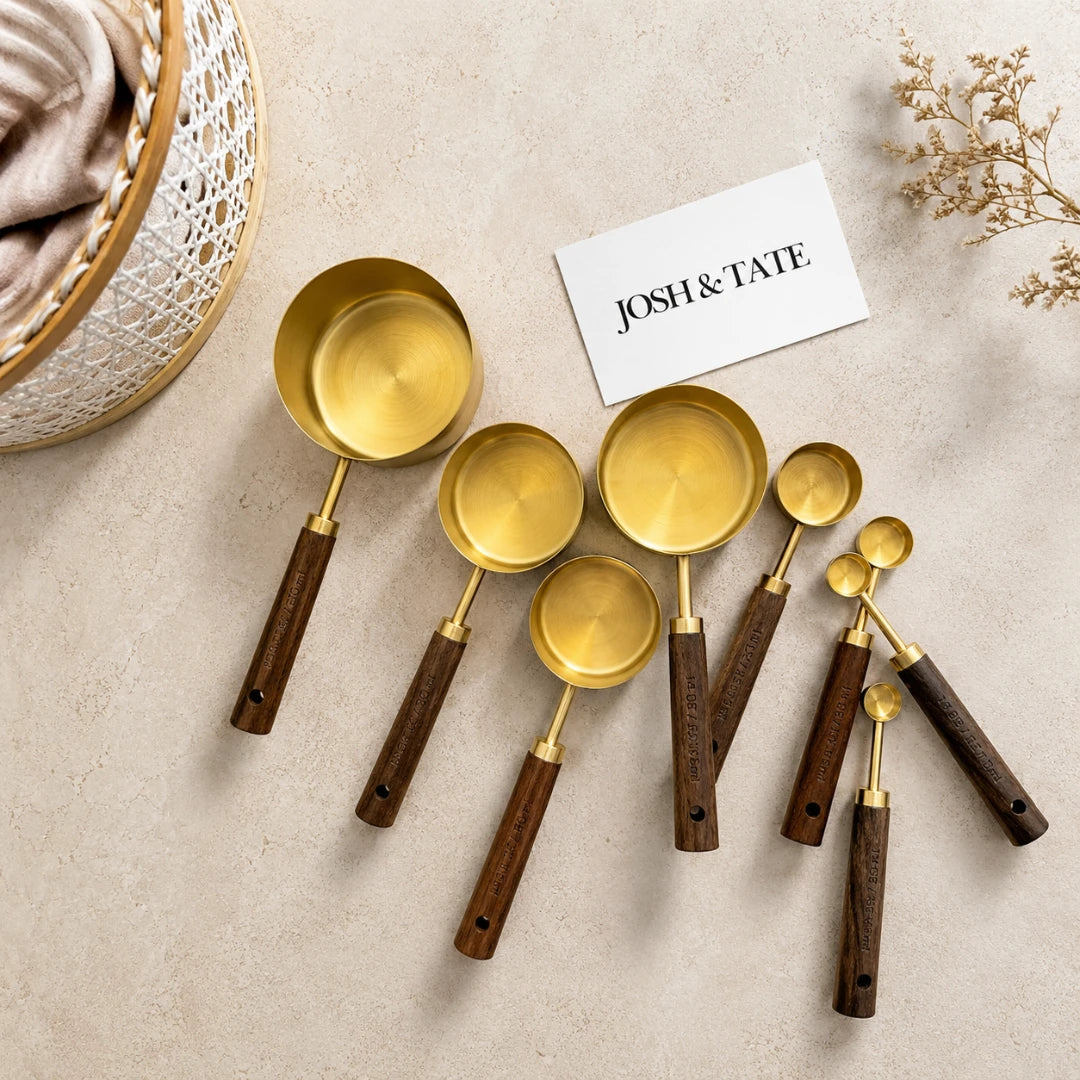 Josh & Tate - Natural Wood Measuring Cup Spoon Set - Set of gold measuring spoons with wooden handles on a beige surface, featuring the brand 'Josh & Tate'.