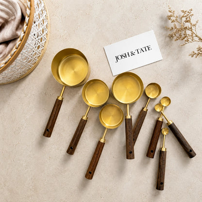 Josh & Tate - Natural Wood Measuring Cup Spoon Set - Set of gold measuring spoons with wooden handles on a beige surface, featuring the brand 'Josh & Tate'.