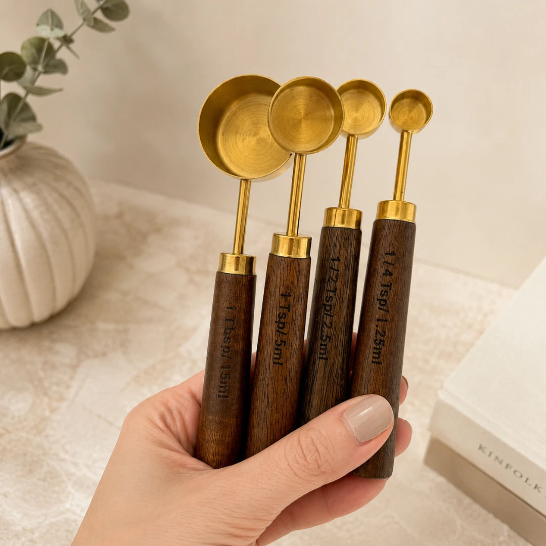 Josh & Tate - Natural Wood Measuring Cup Spoon Set - Set of wooden measuring spoons with gold accents held by a hand on a neutral background.