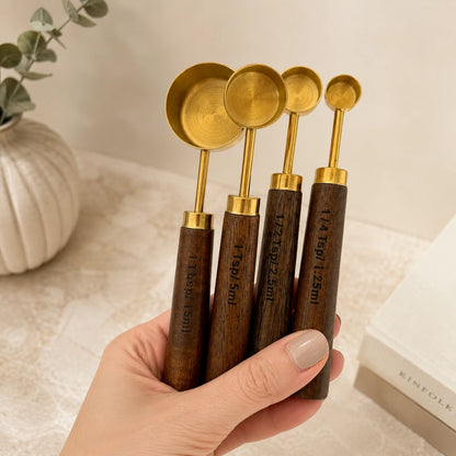 Josh & Tate - Natural Wood Measuring Cup Spoon Set - Set of wooden measuring spoons with gold accents held by a hand on a neutral background.
