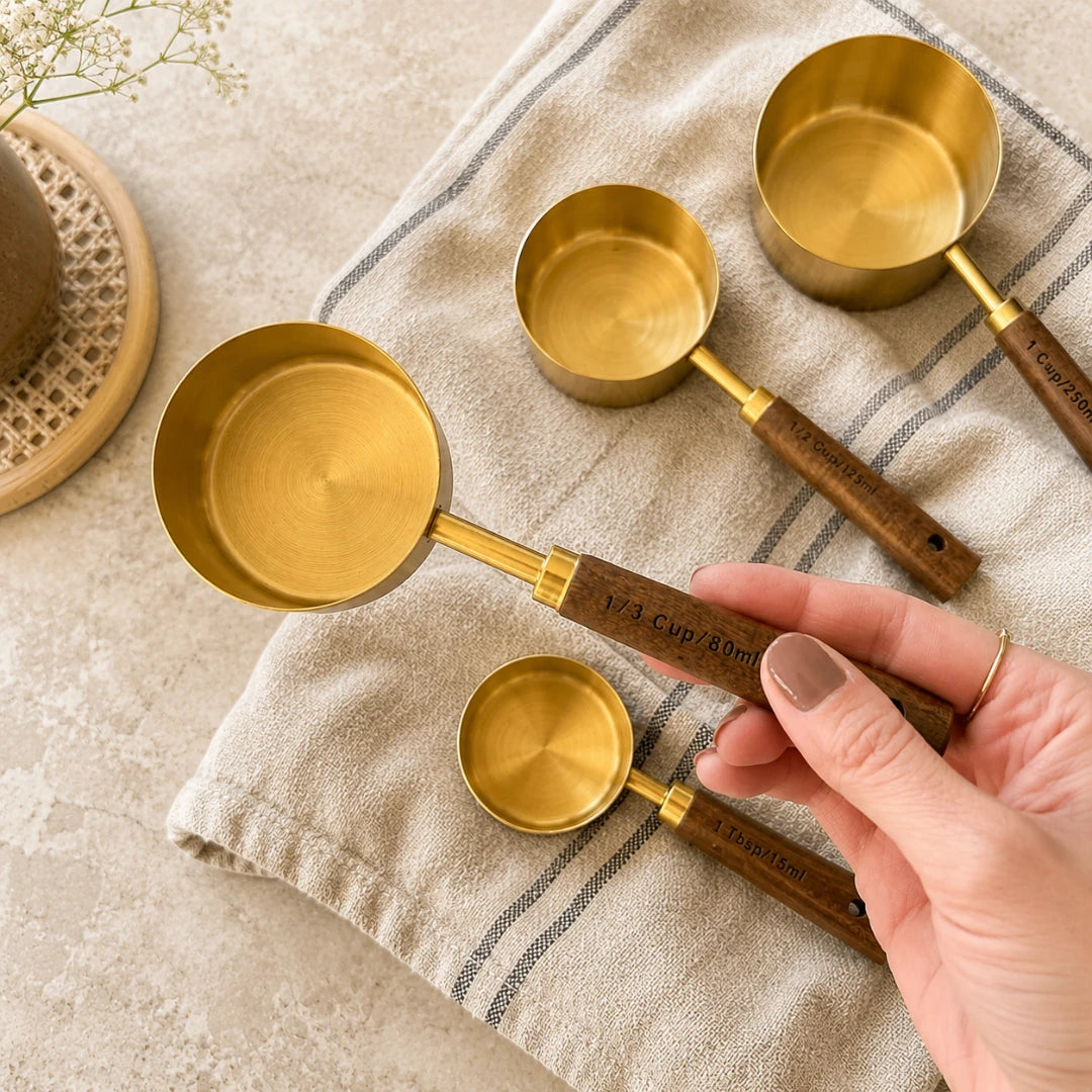 Josh & Tate - Natural Wood Measuring Cup Spoon Set - Set of brass measuring spoons with wooden handles on a textured surface.
