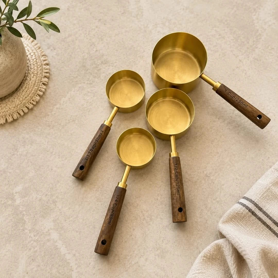 Josh & Tate - Natural Wood Measuring Cup Spoon Set - Set of brass measuring cups with wooden handles on a beige surface.