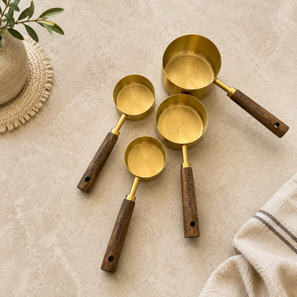 Josh & Tate - Natural Wood Measuring Cup Spoon Set - Set of brass measuring cups with wooden handles on a beige surface.