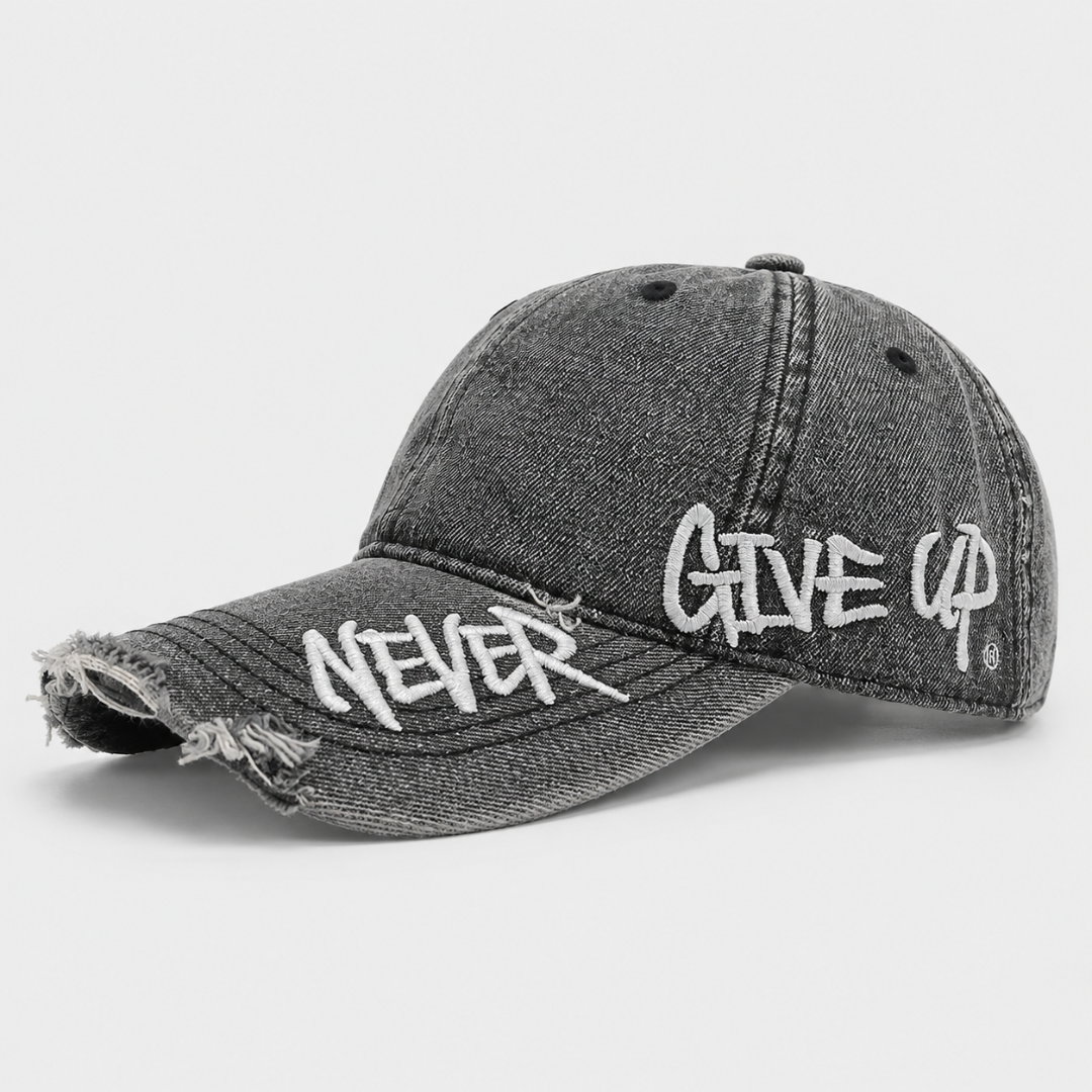 Josh & Tate - NeverGiveUp™ Baseball Cap - A distressed black washed denim baseball cap featuring white embroidered text reading 'NEVER' on the brim and 'GIVE UP' on the side, set against a light gray background.