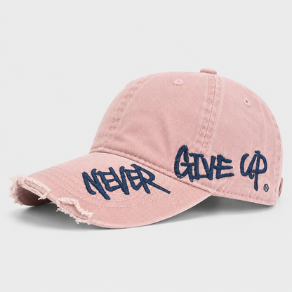 Josh & Tate - NeverGiveUp™ Baseball Cap - A pink distressed baseball cap with navy blue embroidered text reading 'NEVER GIVE UP' on the brim, shown on a light gray background.