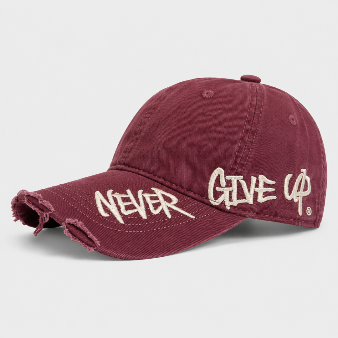 Josh & Tate - NeverGiveUp™ Baseball Cap - A distressed baseball cap in washed burgundy with cream embroidered text reading 'NEVER GIVE UP' on the brim and side, shown on a light gray background.