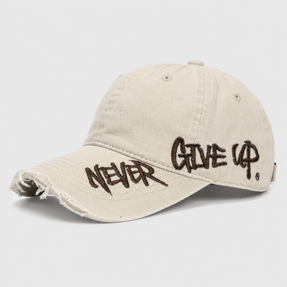 Josh & Tate - NeverGiveUp™ Baseball Cap - A distressed beige baseball cap with dark brown embroidered text reading 'NEVER GIVE UP' on the brim and side, shown on a light gray background.