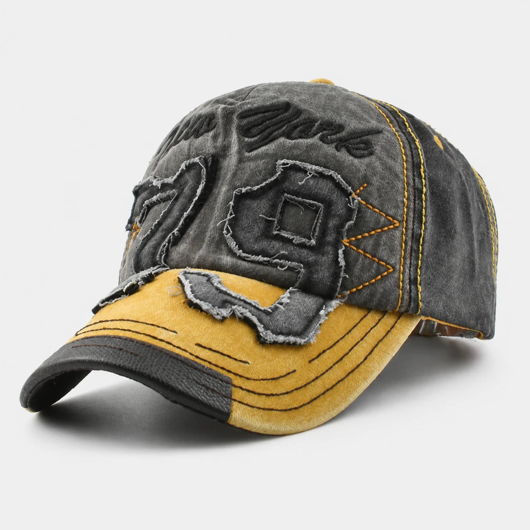 Josh & Tate - NewYork79™ Vintage Cap - A distressed baseball cap featuring a dark gray washed denim front panel with applique patches, a mustard yellow suede-look brim, and yellow contrast stitching, shown on a light gray background.
