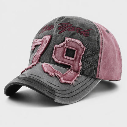 Josh & Tate - NewYork79™ Vintage Cap - A distressed baseball cap featuring a washed dark gray front and brim, dusty rose pink side panels, and large embroidered '79' numbers with frayed edges on the front. The cap is photographed on a clean, light gray background.