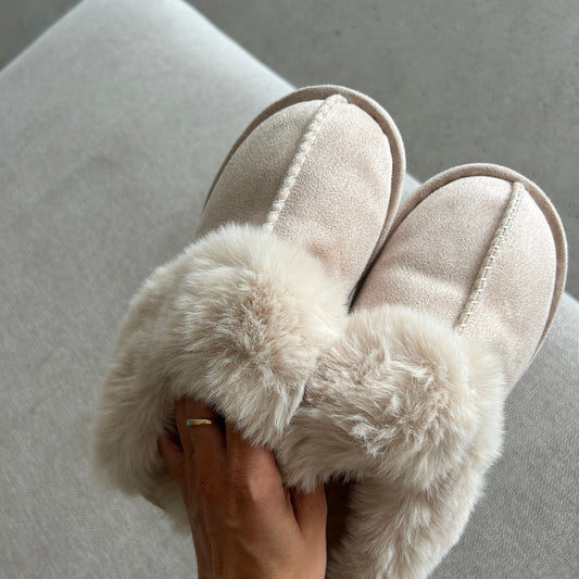 Beige slippers with fluffy fur trim worn by a person on a light gray surface