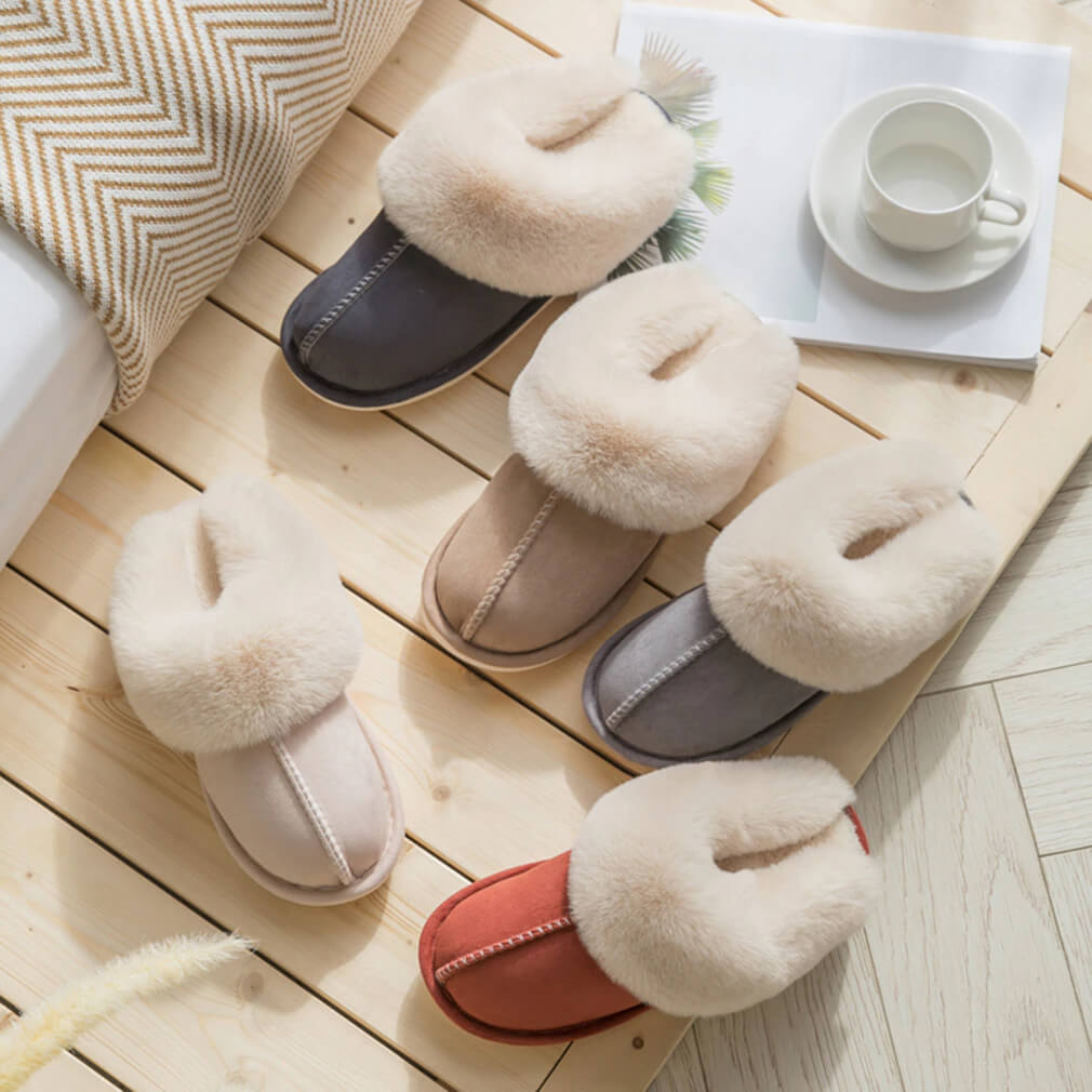 Pair of fluffy slippers on a wooden floor with a cup and saucer in the background.