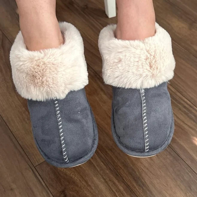 Gray slippers with white fur trim worn indoors on a wooden floor.