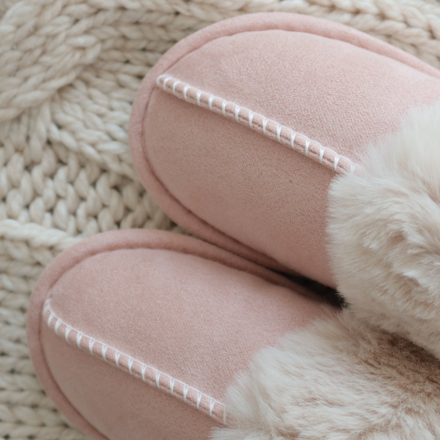 Pair of pink slippers with fur trim on a textured beige surface