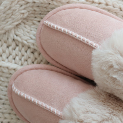 Pair of pink slippers with fur trim on a textured beige surface