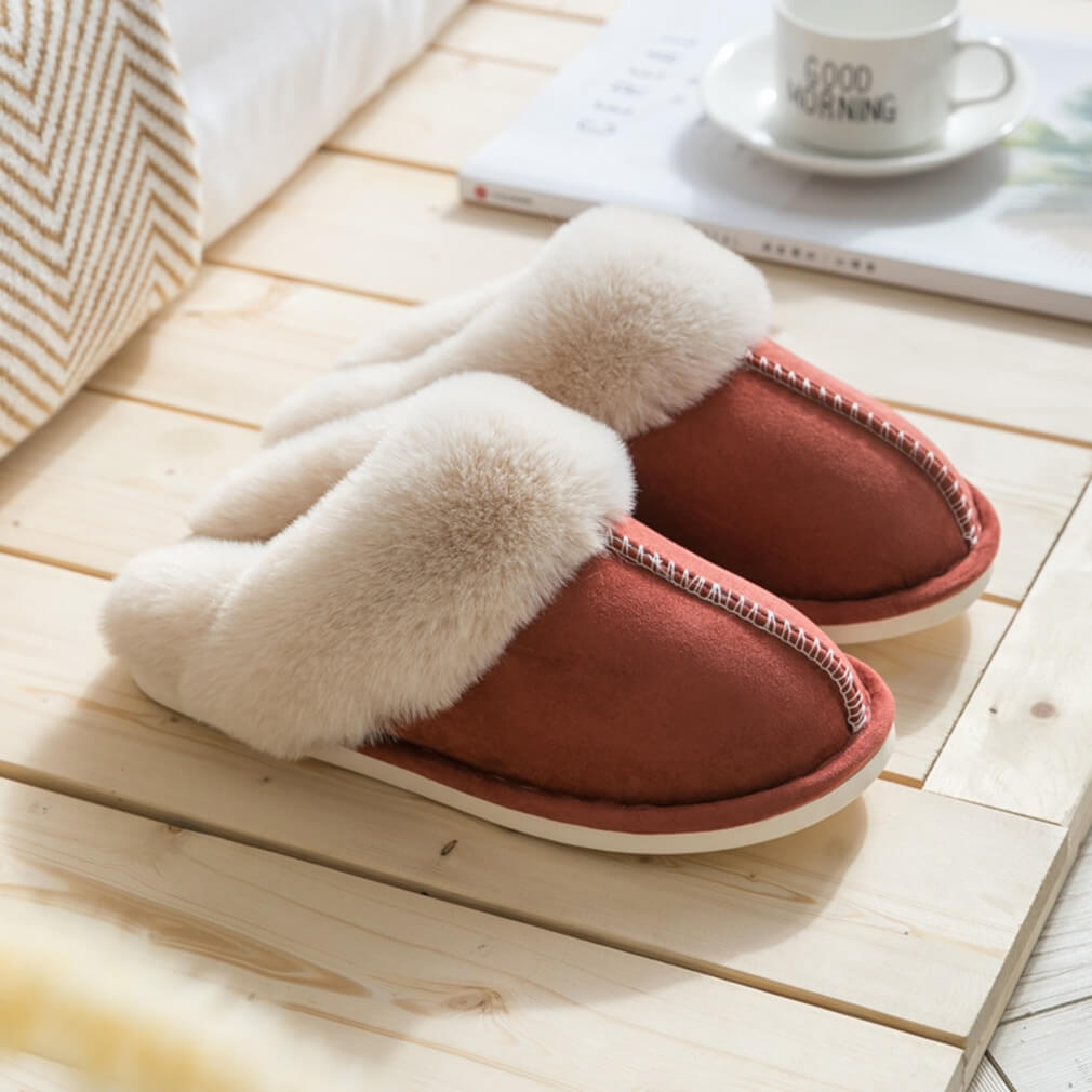 Pair of brown slippers with white fur trim on a wooden floor.