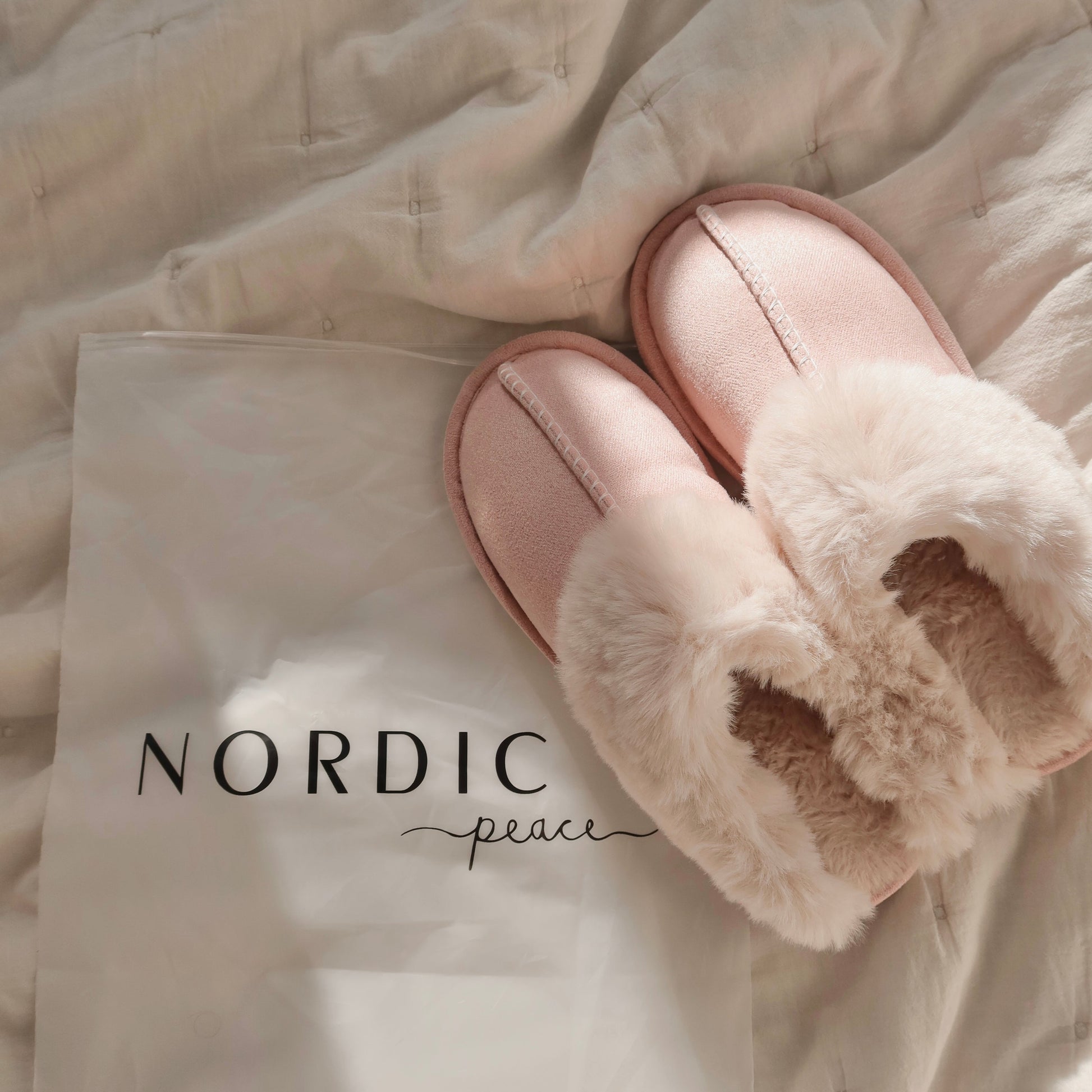 Pink slippers with fluffy interior on a beige blanket, featuring the brand 'Nordic Peace'.