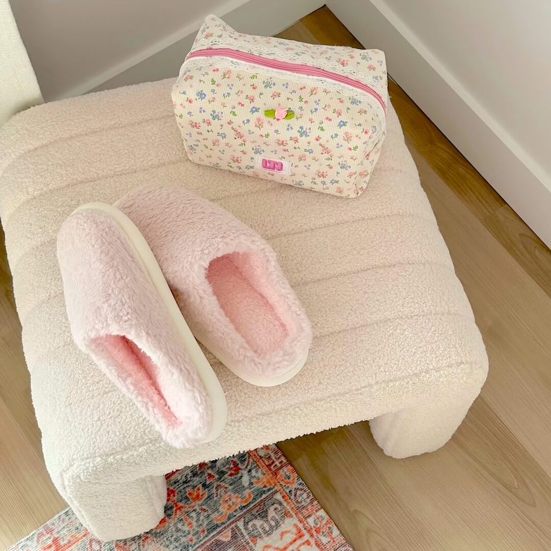 Pink slippers with bunny ears on a white ottoman with a floral-patterned bag.