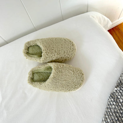 Pair of green slippers on a white surface with a tiled floor background