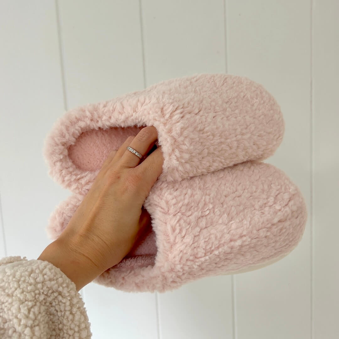 Pink fuzzy slippers held by a hand against a white background