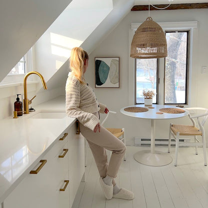 Woman sitting at a kitchen counter in a bright, modern kitchen with white walls and wooden accents.