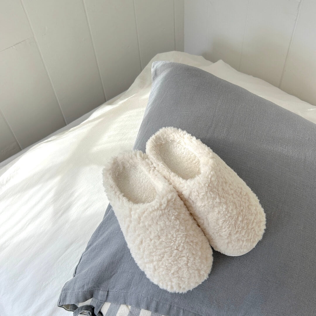 Pair of fluffy white slippers on a gray pillow against a neutral background