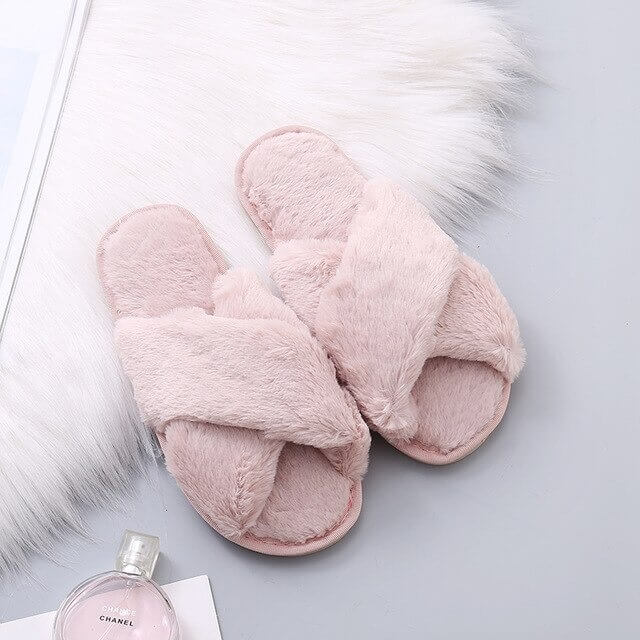 Pair of pink fluffy slippers on a light gray surface with a Chanel perfume bottle.