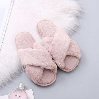 Pair of pink fluffy slippers on a light gray surface with a Chanel perfume bottle.