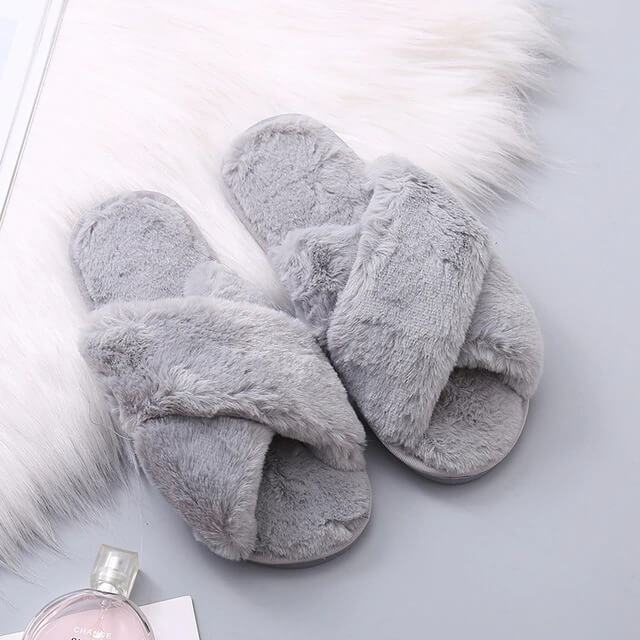 Gray fuzzy slippers on a light gray surface with a small bottle of perfume.